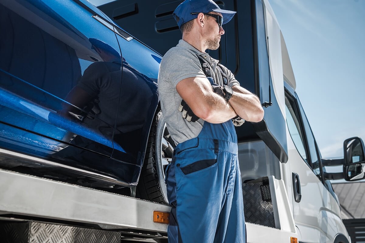 Truck driver in blue overalls standing confidently next to a semi-truck under a clear sky
