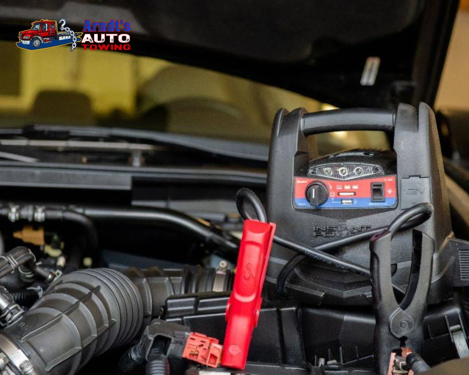 Portable jump starter connected under a vehicle hood by Arndt’s Auto Towing