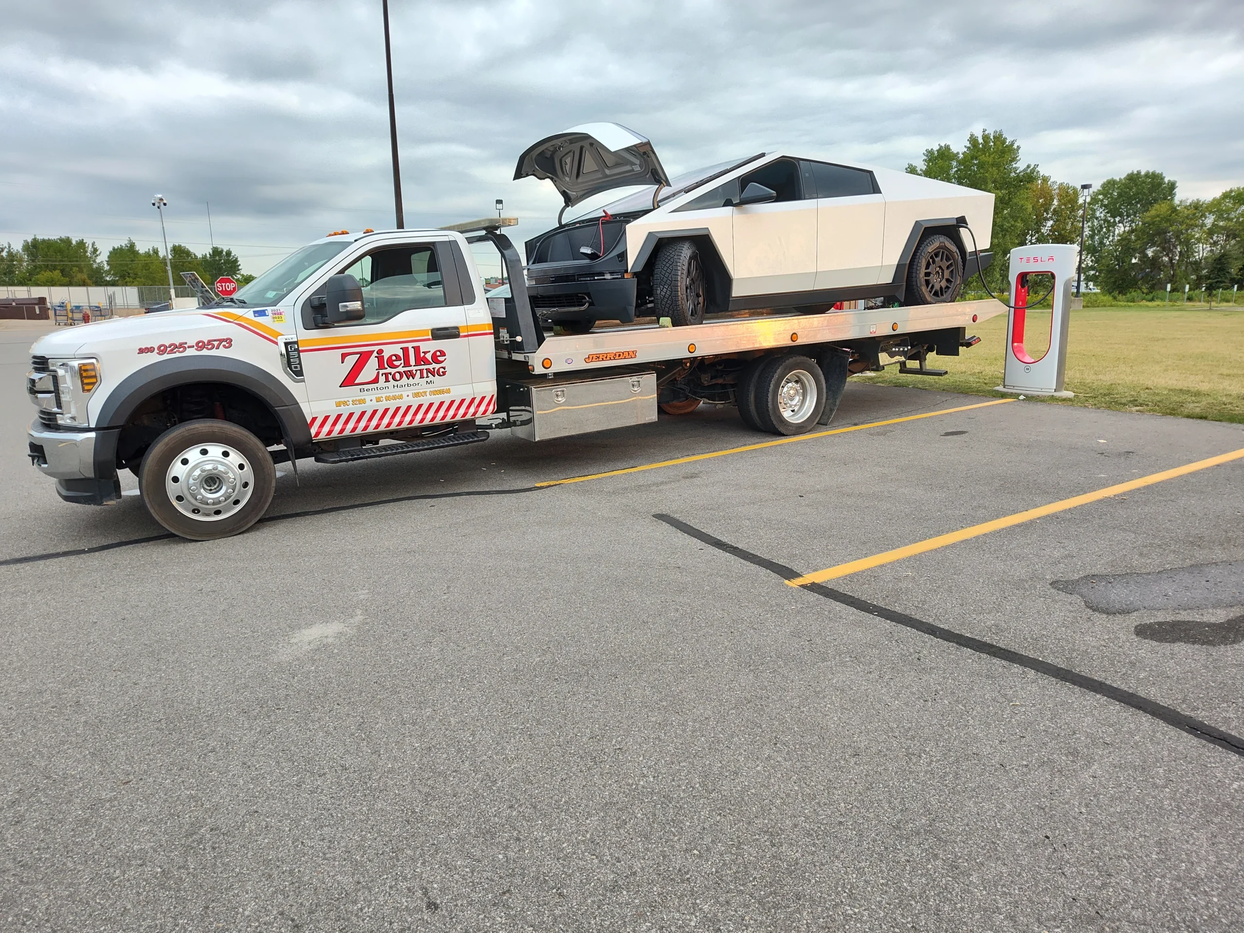 Tesla Cybertruck being towed by Zielke Towing’s light duty flatbed truck near a Tesla charging station