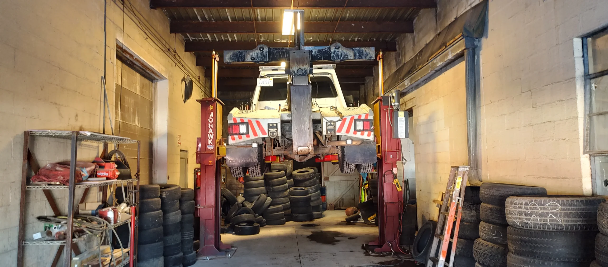 A Zielke Towing tow truck elevated on a Mohawk lift inside the Benton Harbor tire service garage surrounded by replacement tires