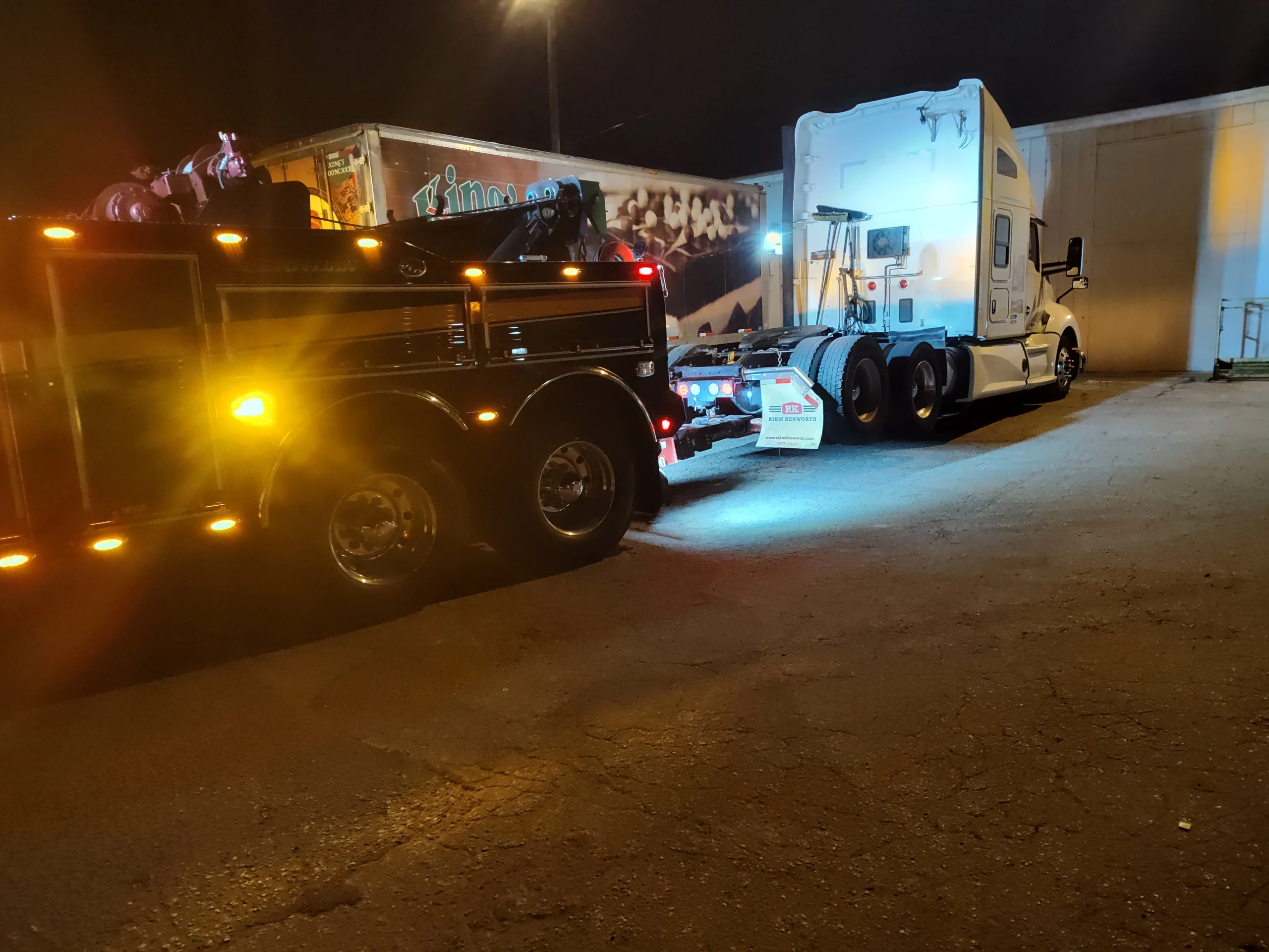 Zielke Towing’s heavy-duty wrecker performing nighttime vehicle electrical diagnostics on a white semi-truck outside a building