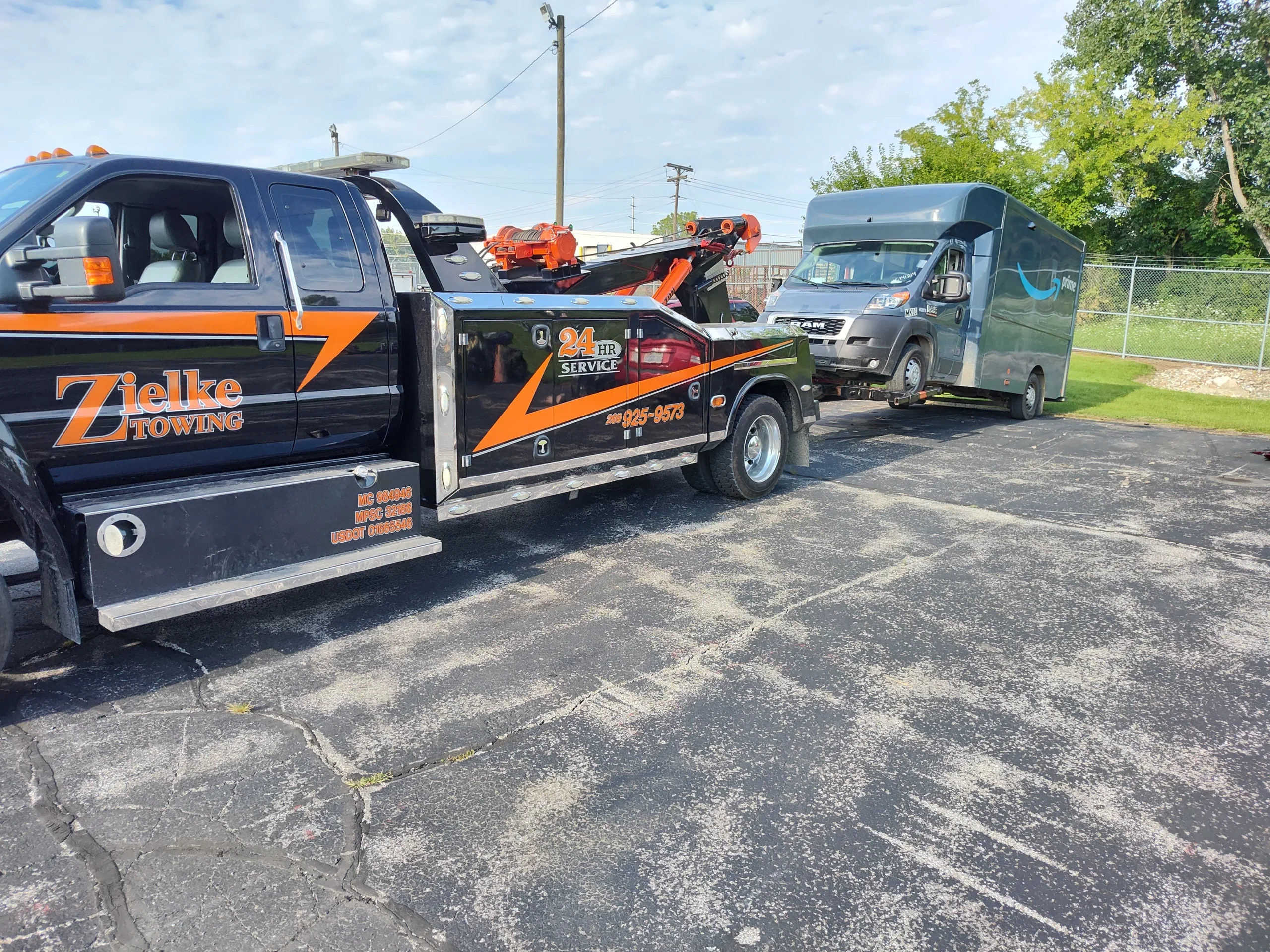Zielke Towing service truck towing a disabled Amazon Prime van in a parking lot under clear skies