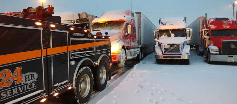 Zielke heavy wrecker assisting a red semi-truck stuck in snow at a truck parking lot during winter