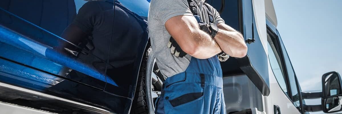 Truck driver in blue overalls standing confidently next to a semi-truck under a clear sky
